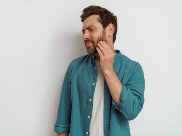 A man is touching his jawline with a look of discomfort on his face