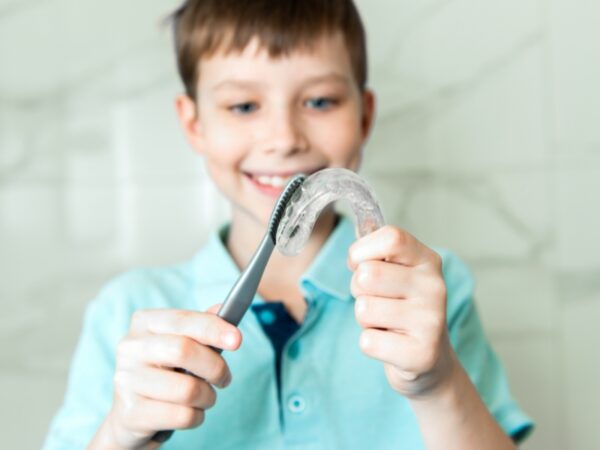 A young boy is using a toothbrush to clean a clear plastic retainer