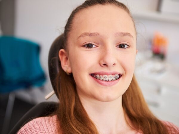 A young girl is smiling to show her braces while sitting in an Orthodontist office.