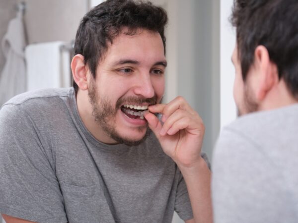 A young man is standing in the bathroom looking at the mirror while placing invisalign aligners on this teeth