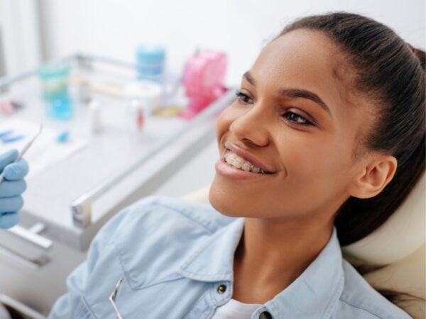 A young woman is wearing braces and smiling while sitting in a chair at the orthodontist office