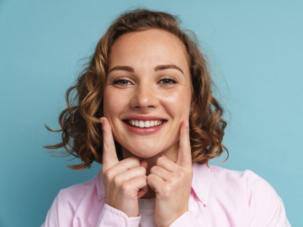 A young woman with curly hair is smiling and her index fingers are touching her jaw line