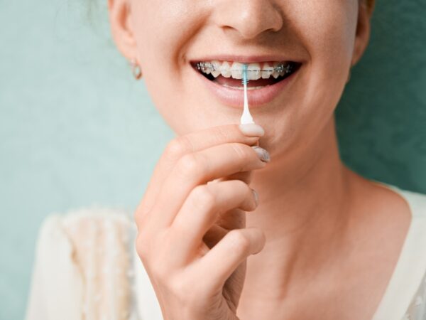 Girl is holding a special flosser brush to clean between her braces and teeth.
