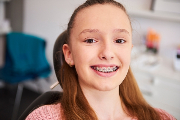 Girl sits in a dentist chair smiling and showing her braces
