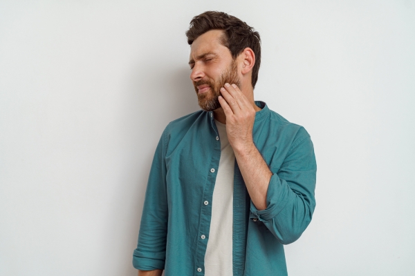 Man holds jaw with a painful look on this face