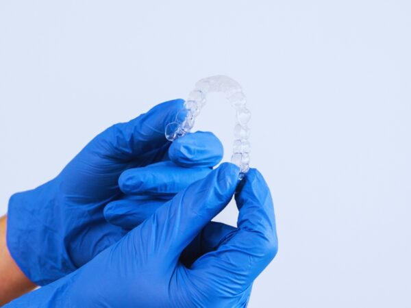 Orthodontist hands wearing blue gloves is holding clear braces