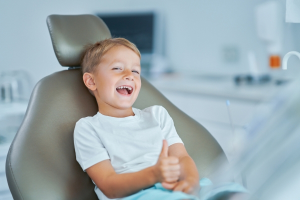 Young boy sits smiling in orthodontist chair with thumb up