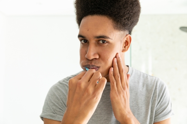 Young man touches his jaw while brushing his teeth