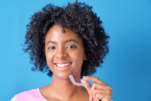 Young woman smiles while holding invisalign aligner in hand