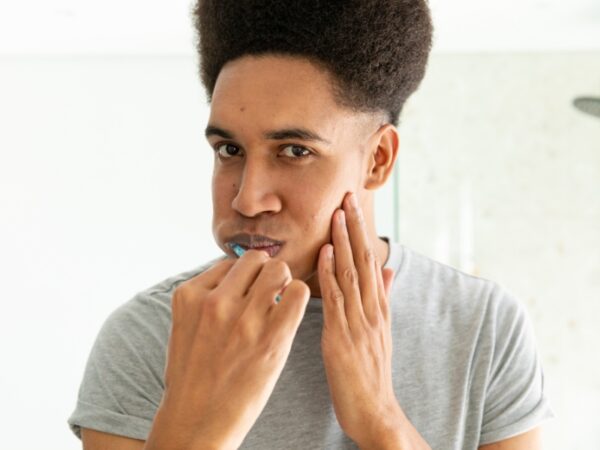 a young man is brushing his teeth while looking at the mirror and has a hand on his jaw